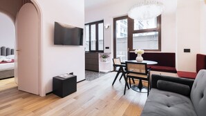 A modern living room with a sofa, a dining table with chairs, a TV mounted on the wall, and a chandelier. - Easylife - Refined apartment near the Duomo (Milano)