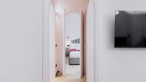 A narrow hallway leading to a bedroom with a bed, a TV mounted on the wall, and a door on the left. - Easylife - Refined apartment near the Duomo (Milano)