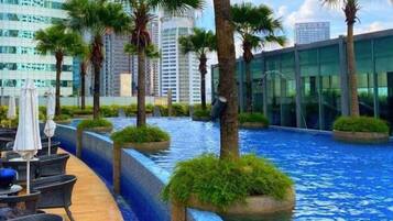 Área de piscina en la azotea con sillones de descanso y palmeras, rodeada de edificios modernos.