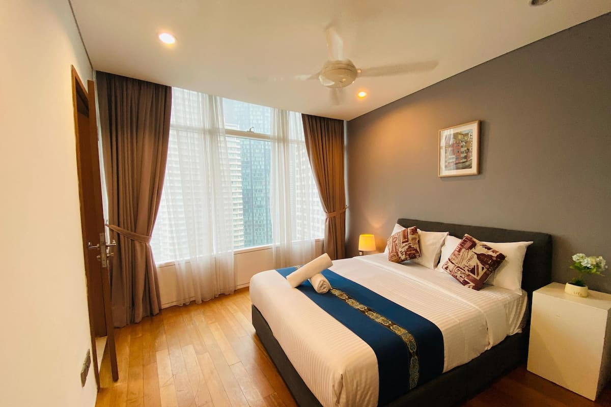 A modern hotel room with a large bed, a ceiling fan, and a view of tall buildings through the window.
