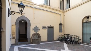 Un patio con un banco de piedra, una cruz y bicicletas aparcadas.