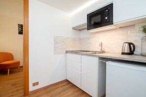 Una cocina compacta con microondas, pileta y tetera, muebles de cocina blancos y piso de madera.