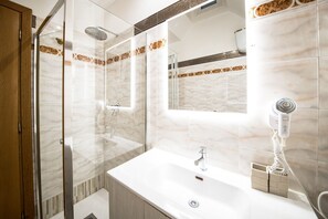 A modern bathroom with a glass shower enclosure, a white sink, and a hairdryer on the wall.