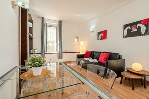 Ein modernes Wohnzimmer mit einem Glastisch, einer schwarzen Ledersofa und einem kleinen Beistelltisch.