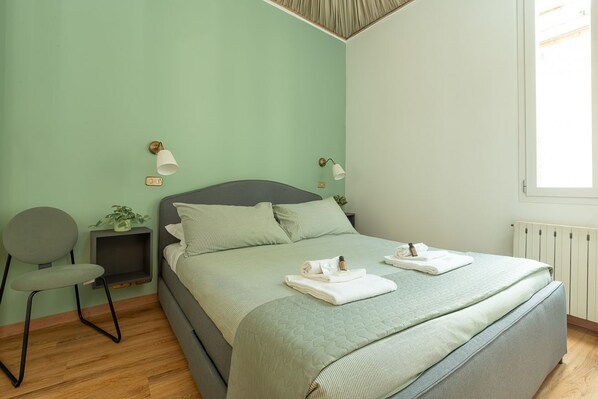 Un dormitorio con cama, mesitas de noche, una silla y una ventana.