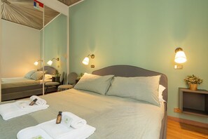A hotel room with a bed, a chair, a small table with a plant, and wall-mounted lights.