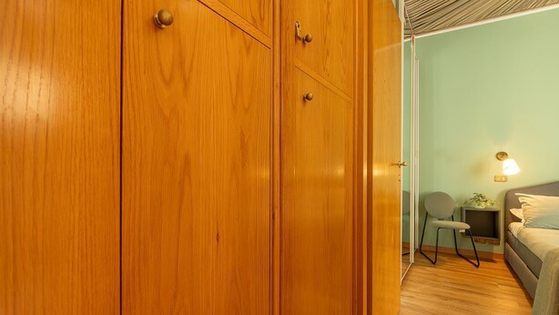 Una habitación con un armario de madera, una cama, una silla y una mesita de noche.