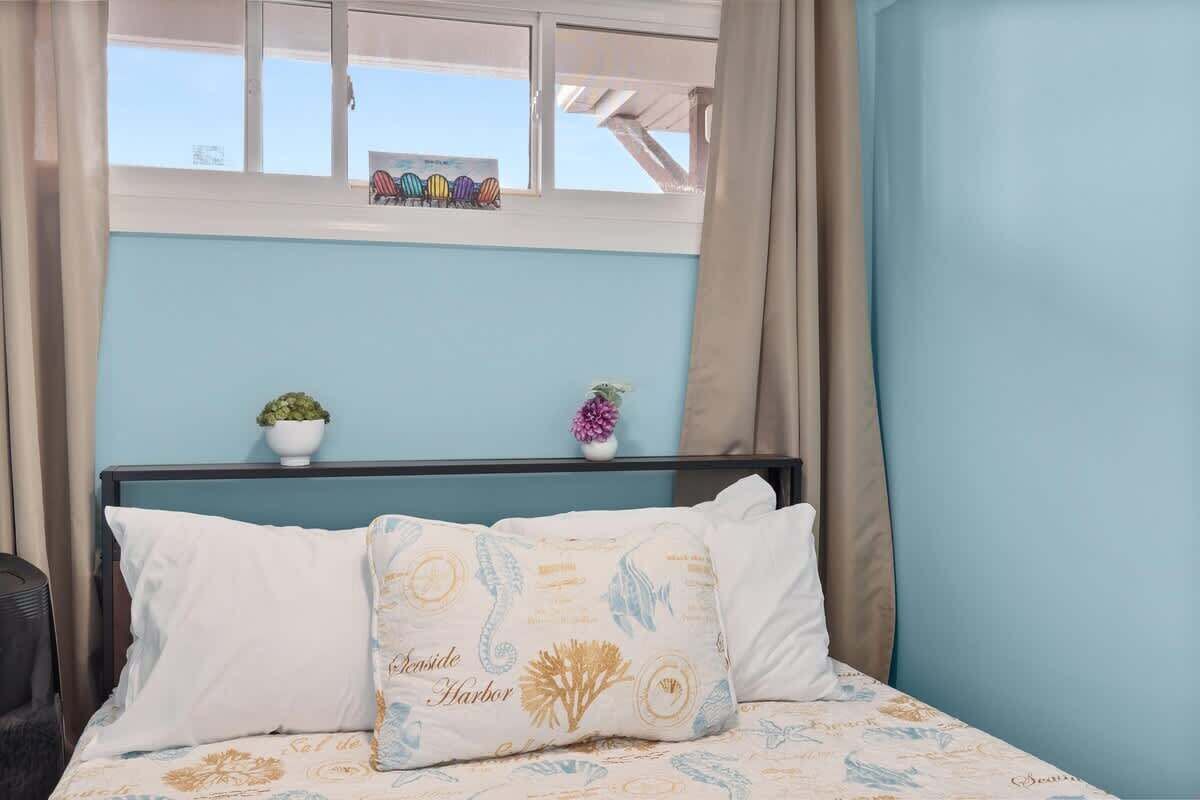 A bedroom with a bed, two pillows, a window, and a small shelf with decorative items.