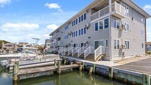 Un edificio de varios pisos frente al agua, con balcones, un muelle y barcos.