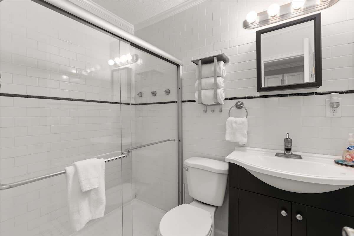 A modern bathroom with a glass shower enclosure, a white toilet, a vanity with a sink, and a mirror.