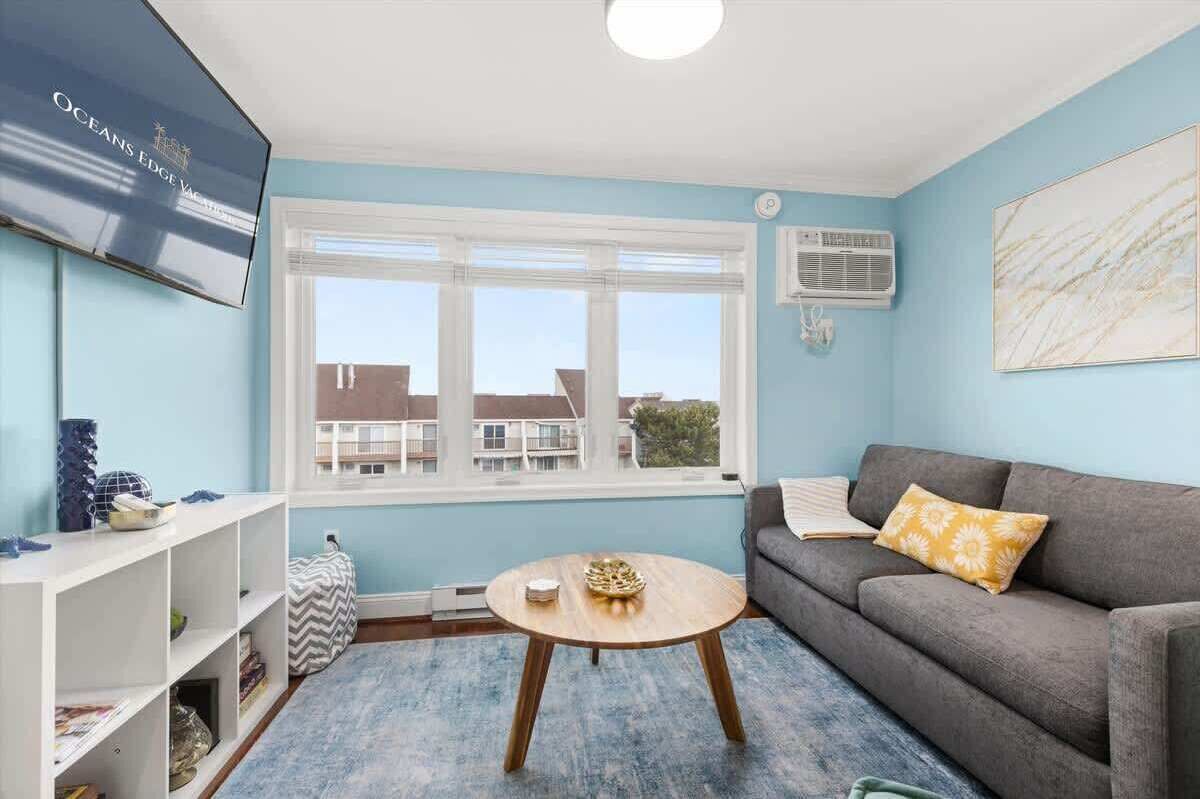 A living room with a blue wall, a grey sofa, a round wooden coffee table, and a TV on the wall.