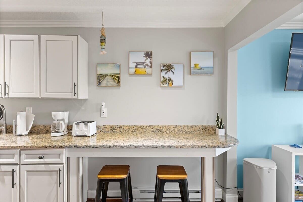 A kitchen with white cabinets, a granite countertop, two stools, and a small potted plant.