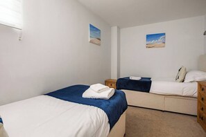 A room with two beds, each with a blue and white duvet, a wooden nightstand, and a small table. - Modern, Dog friendly, 2 Bedroom Beach Front Apt. Central Newquay (Newquay Cornwall)