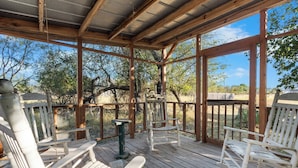 Une terrasse extérieure couverte, dotée de bancs en bois et d’une table, entourée d’arbres et offrant une vue sur un ciel dégagé.