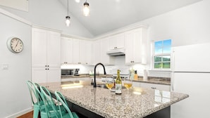 Cocina moderna con armarios blancos, encimera de granito, horno empotrado y ventana con vistas a zonas verdes.