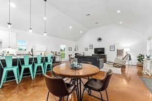 Un vaste espace de vie comprenant une table à manger ronde en bois, des chaises de couleur turquoise, un canapé gris et une cheminée.