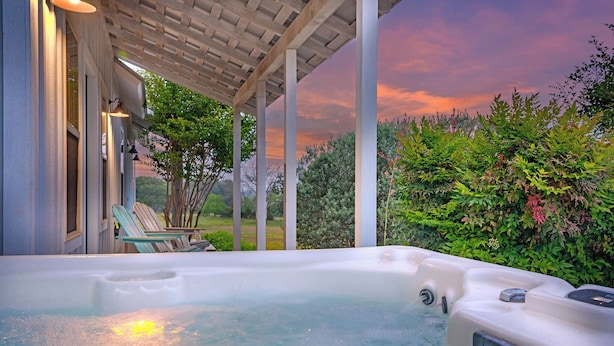 Un jacuzzi bajo una pérgola con vistas a un jardín y al atardecer.