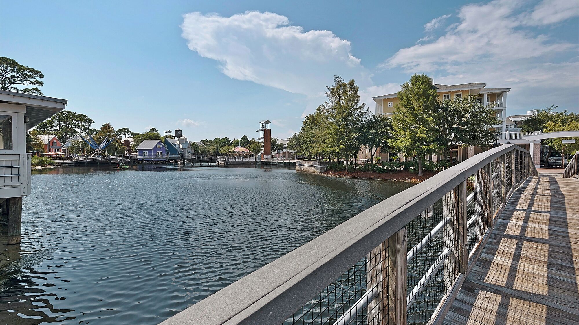 A riverside walkway with a bridge, buildings, and trees.