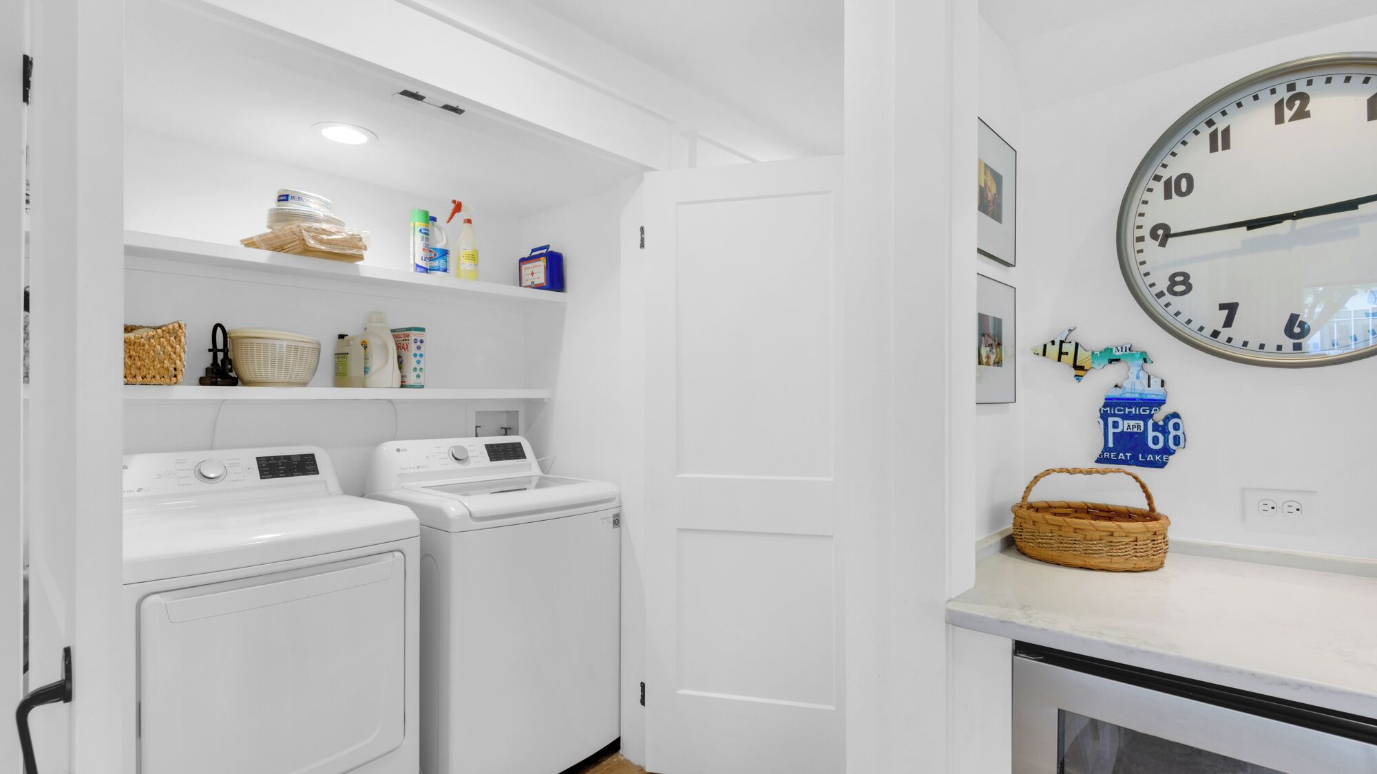 A laundry room with two front-loading washing machines, a drying rack, and shelves with laundry supplies.