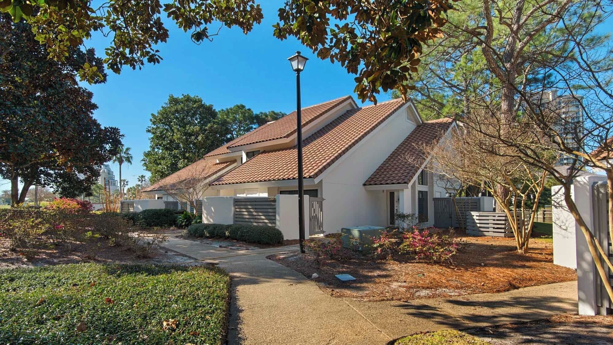 A residential area with a house featuring a tiled roof, a paved driveway, and a well-maintained garden with shrubs and flowering plants.