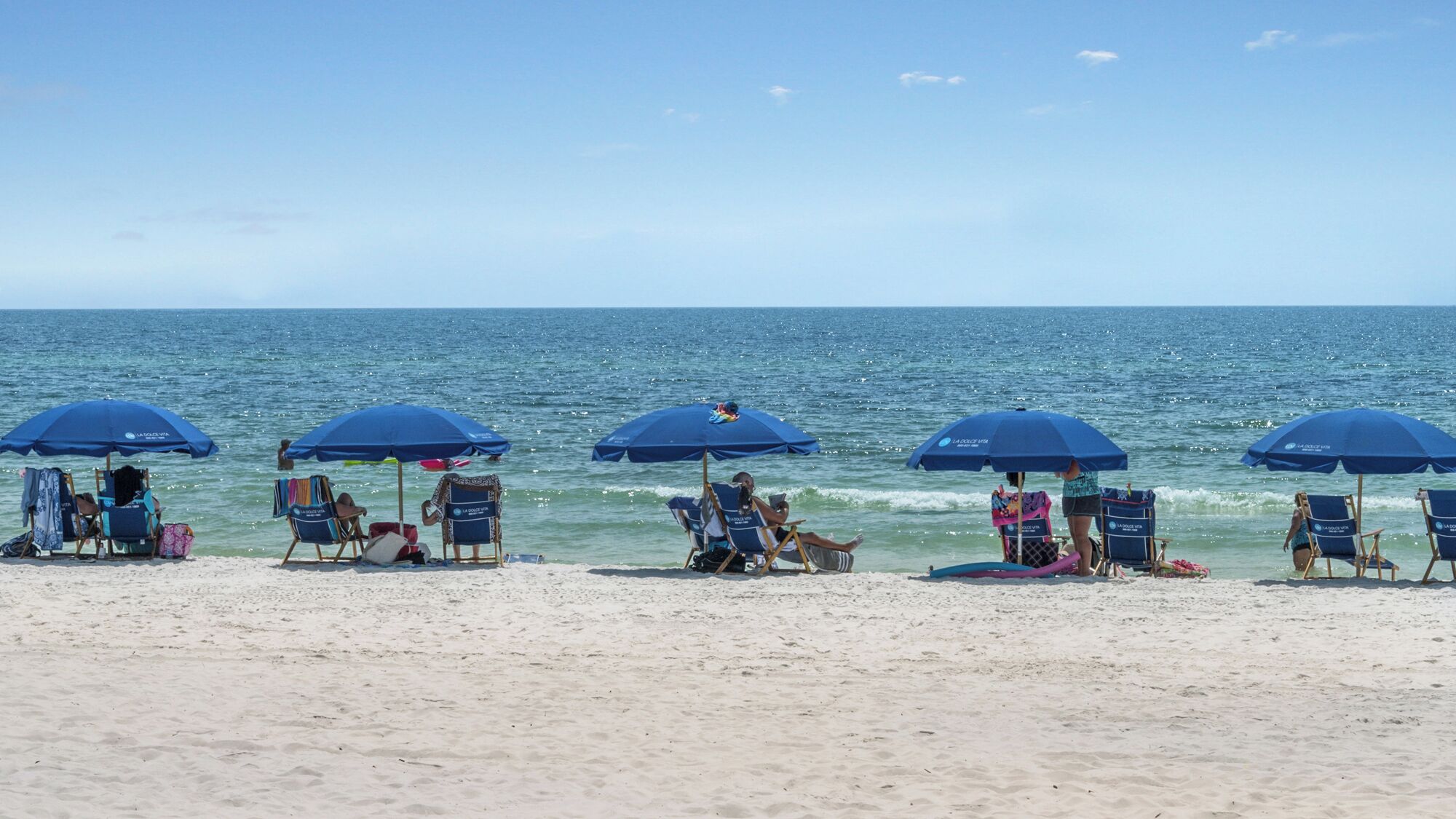 A beach with multiple blue umbrellas and beach chairs.