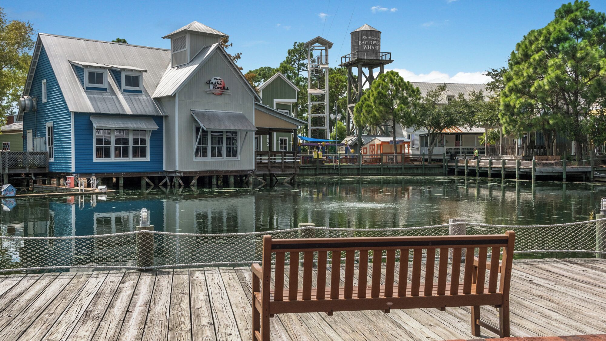 A waterfront building with a dock, a wooden bench, and a water tower.