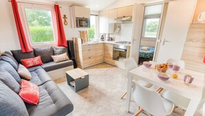 A compact living space with a sofa, dining table, kitchenette, and a small bed. - Bungalow, terrace, garden, 200m from the beach, by Groom*. (Guidel)