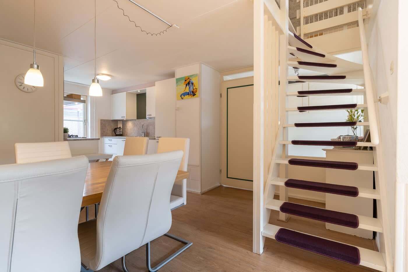 Un interior moderno con comedor, cocina y una escalera de madera.