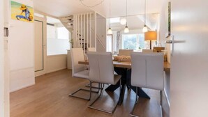 A dining area with a wooden table, four chairs, pendant lights, and a staircase leading to another level. - Apartment with balcony in Veere | Buiten de Veste 36 (Veere)