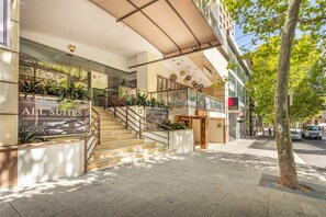 L’entrée d’un hôtel, avec un escalier menant au hall d’accueil, des portes vitrées et une enseigne indiquant « All Suites Perth ».