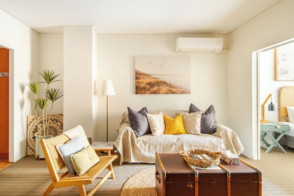 A cozy living room with a sofa, a wooden chair, a small table, and a suitcase.