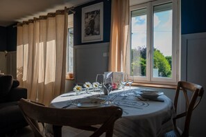 Un área de comedor con una mesa lista para dos personas, una ventana con cortinas y un cuadro en la pared.