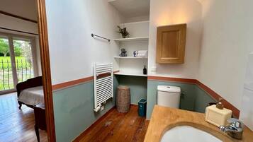 Une salle de bain avec un plancher en bois, un lavabo blanc, des toilettes et une étagère contenant des articles de toilette.