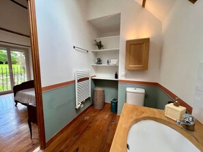 Un baño con piso de madera, un lavamanos blanco, un inodoro y un estante con artículos de aseo.