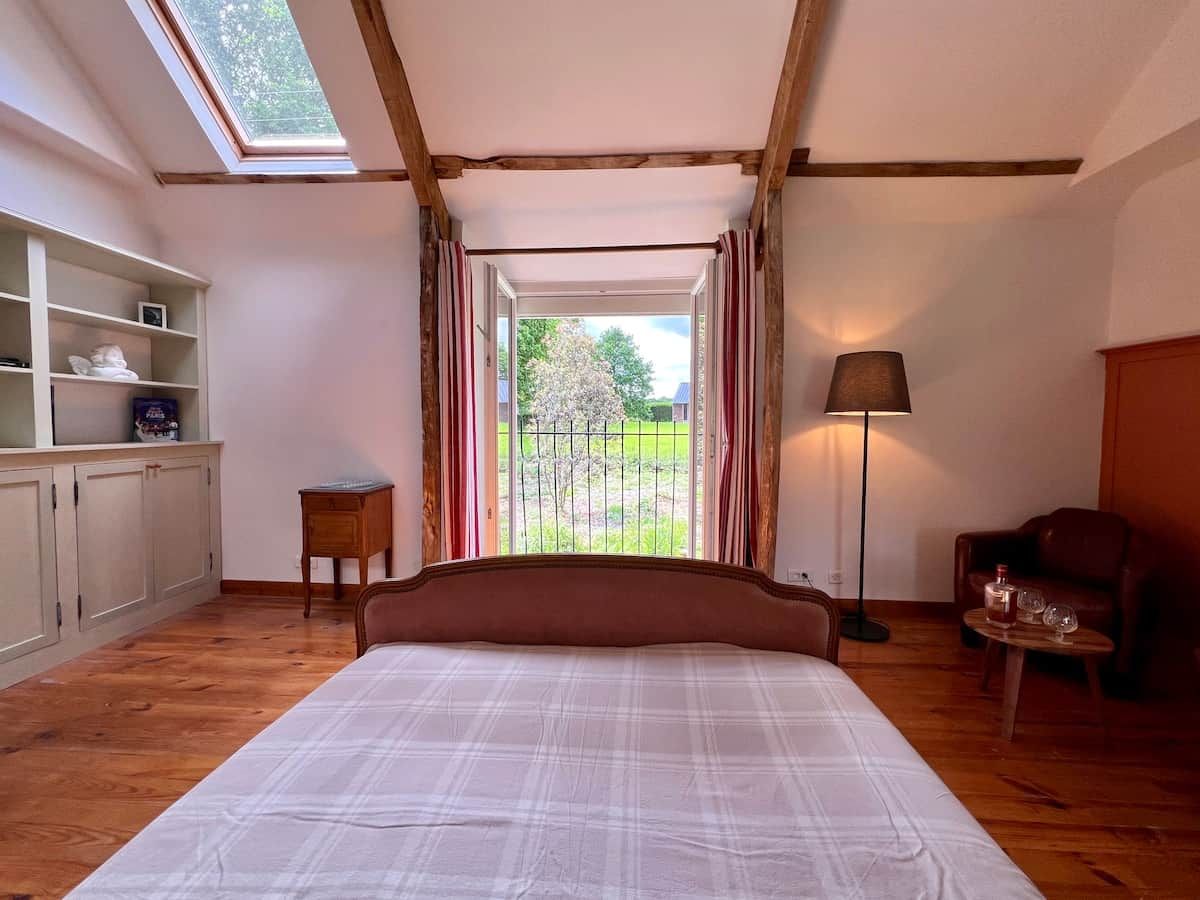 Un dormitorio con una cama grande, una mesita de noche, una lámpara, una silla y vistas al exterior a través de una ventana.