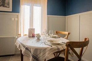 A dining area with a table set for two, a radiator, and a window with curtains.