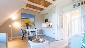 Una cucina moderna con mobili bianchi e un forno a microonde, una zona pranzo con tavolo e sedie, e una scala che conduce a un altro piano.