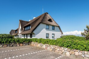 A two-story house with a thatched roof and white walls, surrounded by a stone wall and greenery. - Wattblick. Rantum. Strandkorb (Rantum)
