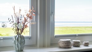 Una finestra con vista sul mare, un vaso con piante secche e tre cesti intrecciati sul davanzale.