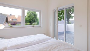 Een slaapkamer met twee bedden, grote ramen en een schuifpui naar een balkon.