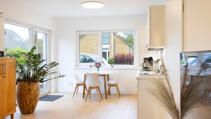 Een moderne keuken met witte kasten, een eethoek met een ronde tafel en stoelen, en grote ramen met uitzicht op buiten.
