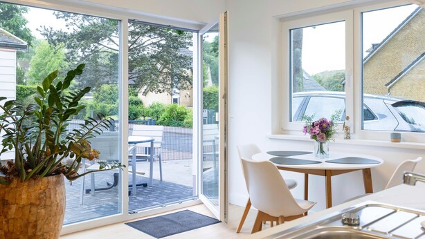 Een moderne keuken met een groot raam, een eethoek met witte stoelen en een potplant.