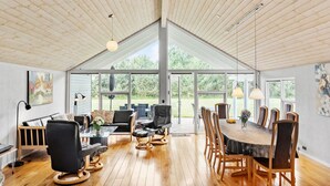 Ein geräumiges Zimmer mit hoher Decke, großen Fenstern und einer Essecke mit Holztischen und -stühlen.