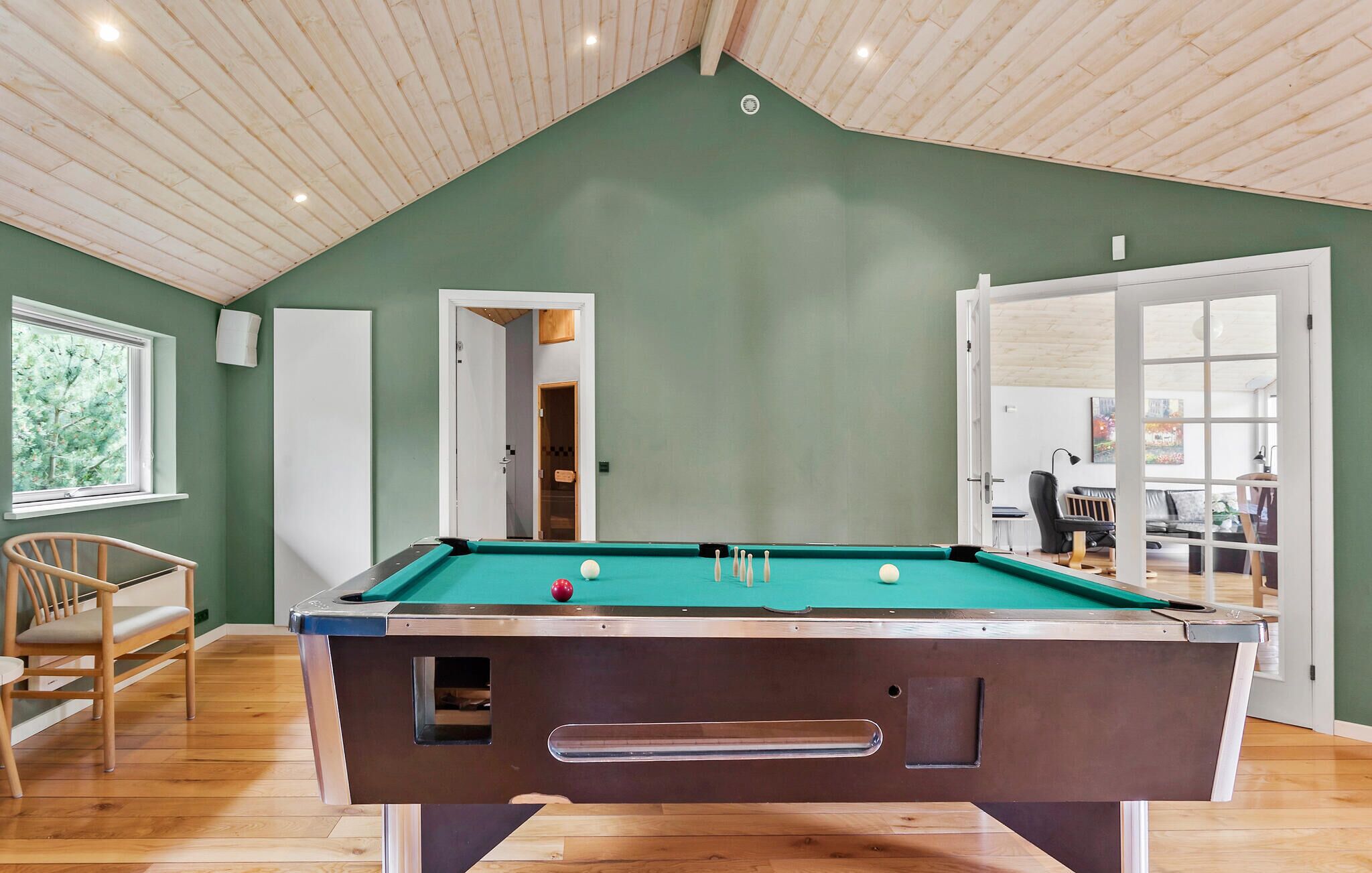 Een biljarttafel in een ruimte met groene wanden, houten vloeren en een schuin dak.