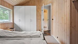 Ein Schlafzimmer mit Holzbalkendecke, einem Bett mit weißer Bettwäsche, einem Fenster und einem Kleiderschrank.