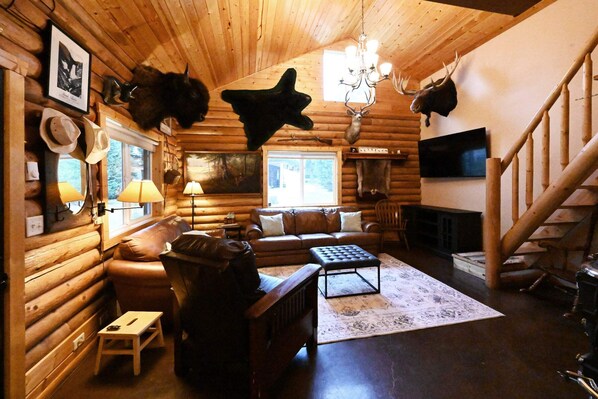 A log cabin interior with a fireplace, leather sofa, and mounted animal heads. - Cabin of Hygge: 19 Miles to Yellowstone (Island Park)
