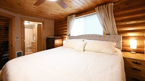 A wooden cabin bedroom with a bed, a ceiling fan, a nightstand, and a window with curtains. - Cabin of Hygge: 19 Miles to Yellowstone (Island Park)