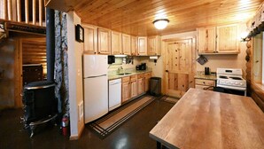 A wooden cabin kitchen with a stove, sink, and cabinets. - Cabin of Hygge: 19 Miles to Yellowstone (Island Park)