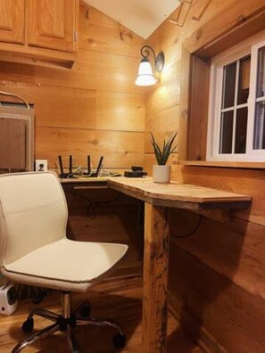 Un interior de madera con una silla de oficina blanca, una mesita y una planta en maceta.