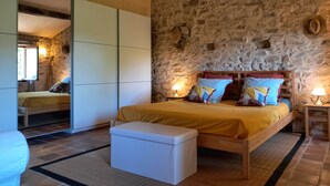 Un dormitorio con pared de piedra, una cama de madera con un banco, una mesita de noche con una lámpara y un armario.